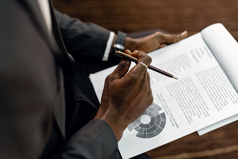 A businessman in a suit reviewing printed documents with a pen, focusing on details.